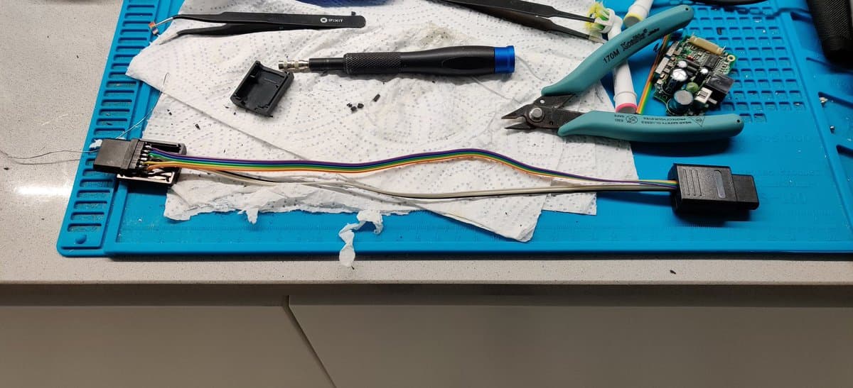 FDSStick transfer cable in progress on blue mat: connectors, multicolored wires, soldering iron, tweezers, and circuit board components on white work surface.