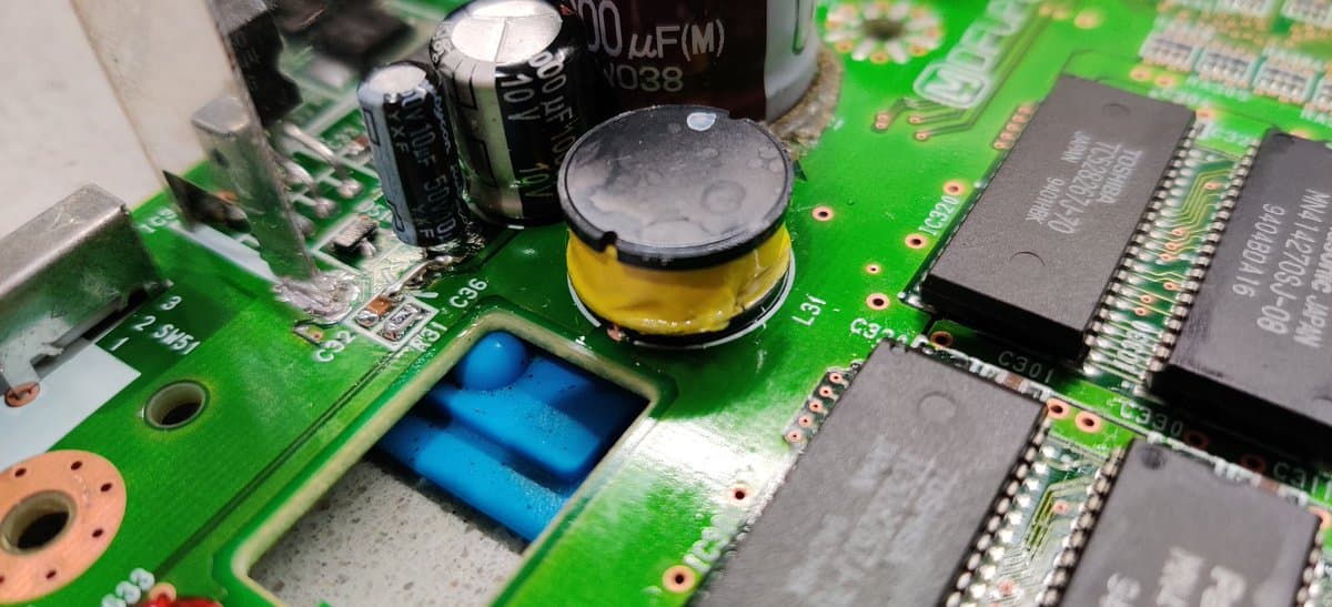 Closeup of 3DO Panasonic FZ-1 motherboard showing ceramic capacitor near C36 with missing trace connection, alongside electrolytic capacitors and IC chips on green PCB.