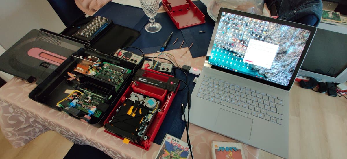 Homemade FDSStick transfer cable with exposed circuit boards and connectors on workbench next to laptop displaying disk images.