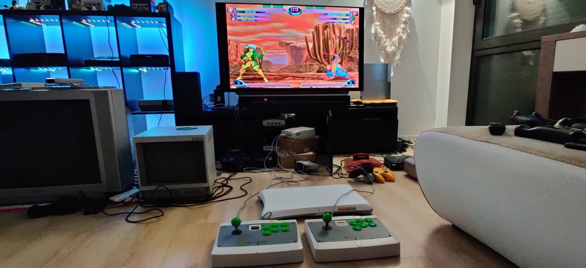 Dreamcast arcade stick with green joystick and buttons on workbench, Marvel vs Capcom 2 displaying on CRT monitor during testing.