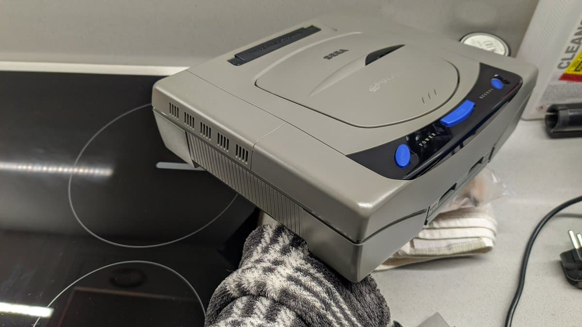 Retrobrighted Sega Saturn model 1 shell displayed on workspace, showing restored plastic casing next to monitor and work area.