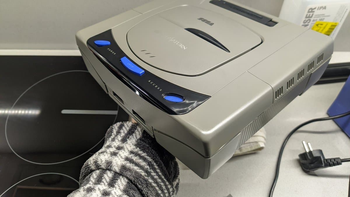 Retrobrighted Sega Saturn model 1 NTSC-J console displaying restored cream-colored shell next to disk drive and power cable on work surface.