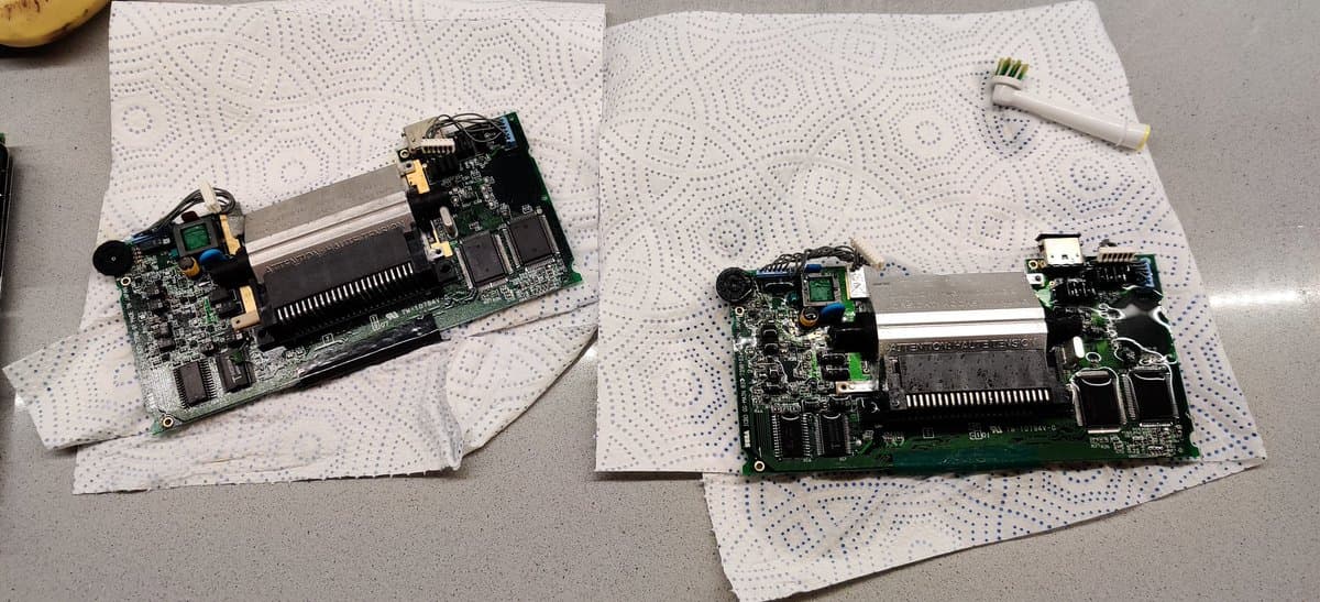 Two Sega Game Gear mainboards on antistatic mats during restoration, showing corrosion damage and loose components from electrolyte contamination.