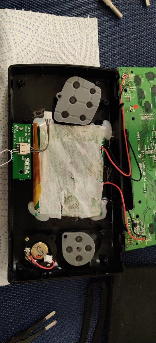 Sega Nomad internals showing aftermarket screen secured with napkin insulation, green circuit boards visible, kapton tape repair in progress.