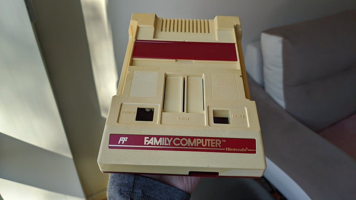 Nintendo Famicom top view showing cartridge slot, controller ports, power and reset buttons with composite mod board installed and new red/white sticker.