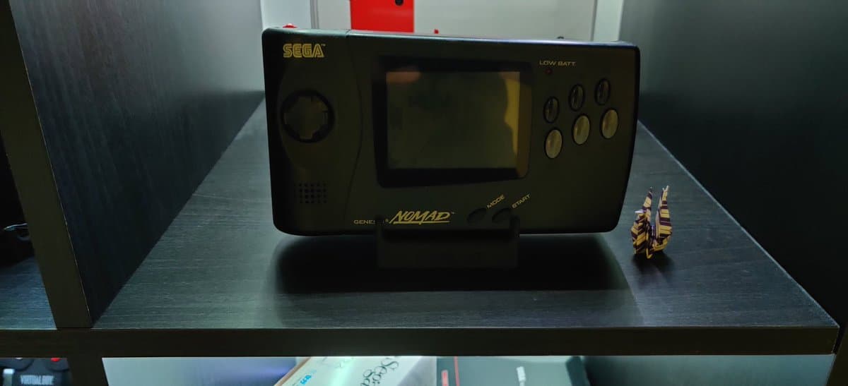 Restored Sega Nomad handheld console on display stand with repaired aftermarket screen, shown from front angle with functional controls visible.