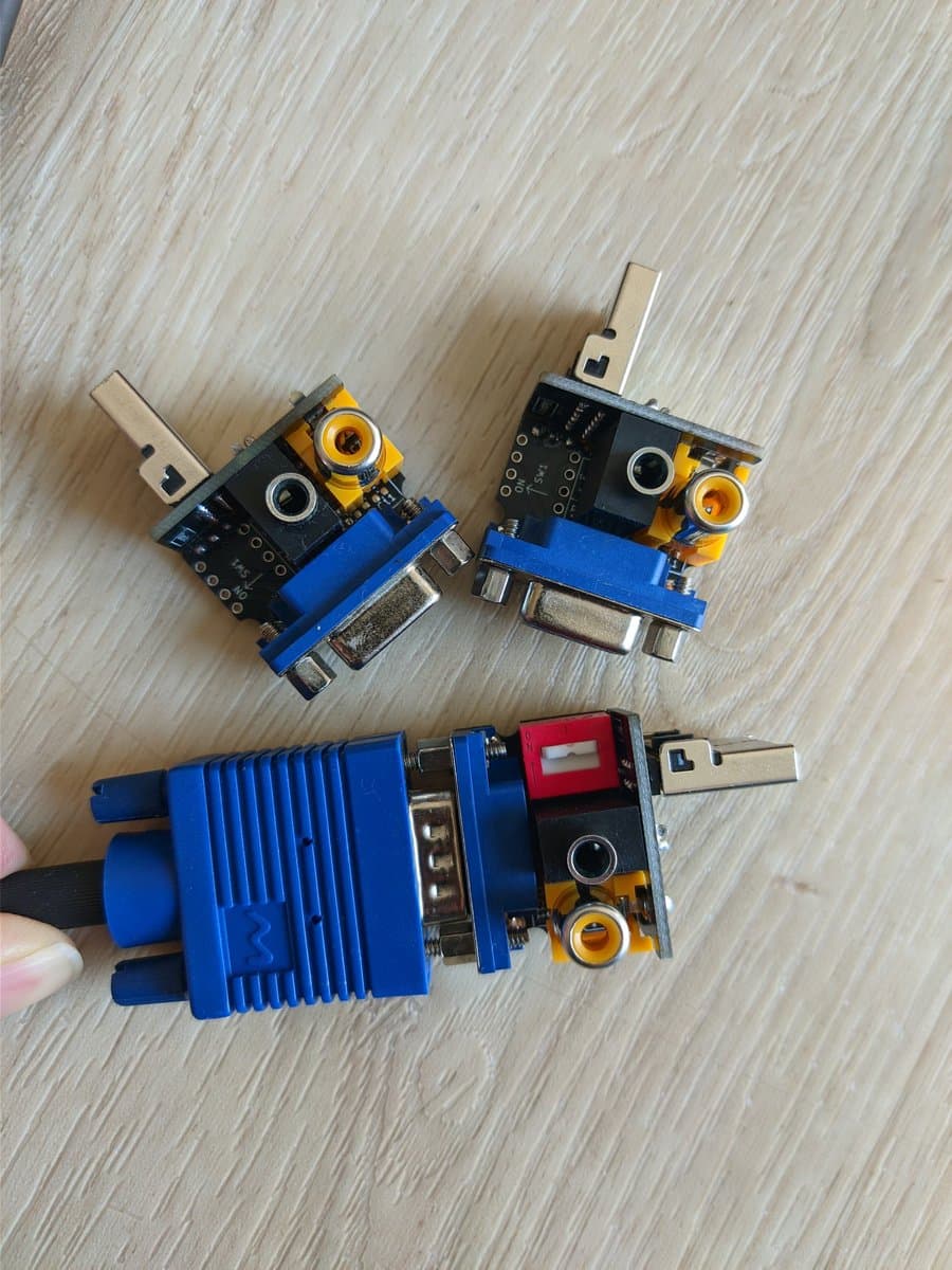 Three Jeff Chen VGA dongles displayed on wooden surface: two assembled units with blue connectors and yellow optical components, one with blue heat sink attached.