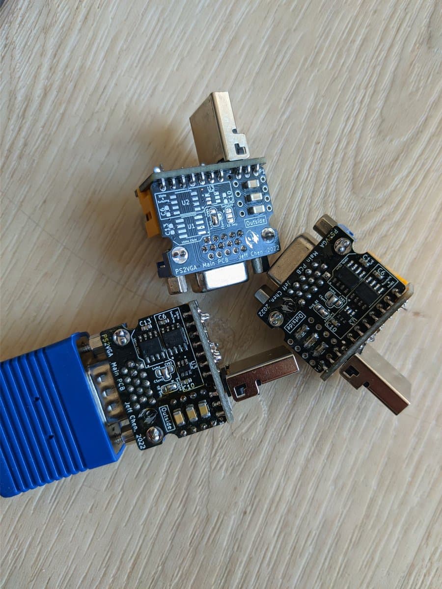 Three Jeff Chen VGA dongles displayed on wooden surface: PS2VGA Main PCB with USB connector, and two black driver boards with various components and connectors.