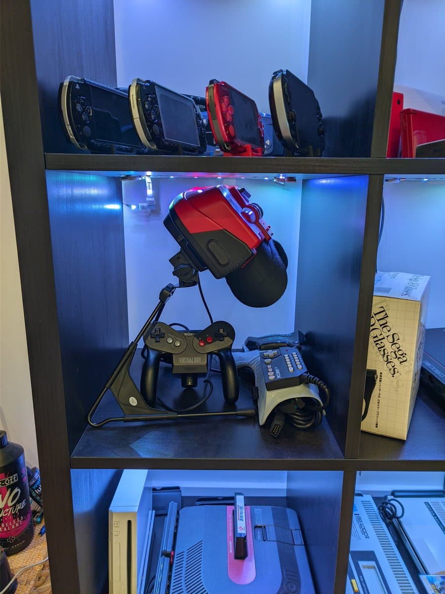 Nintendo Virtual Boy with red Repair Box stand displayed on shelf with controllers, power supply, and game cartridges.