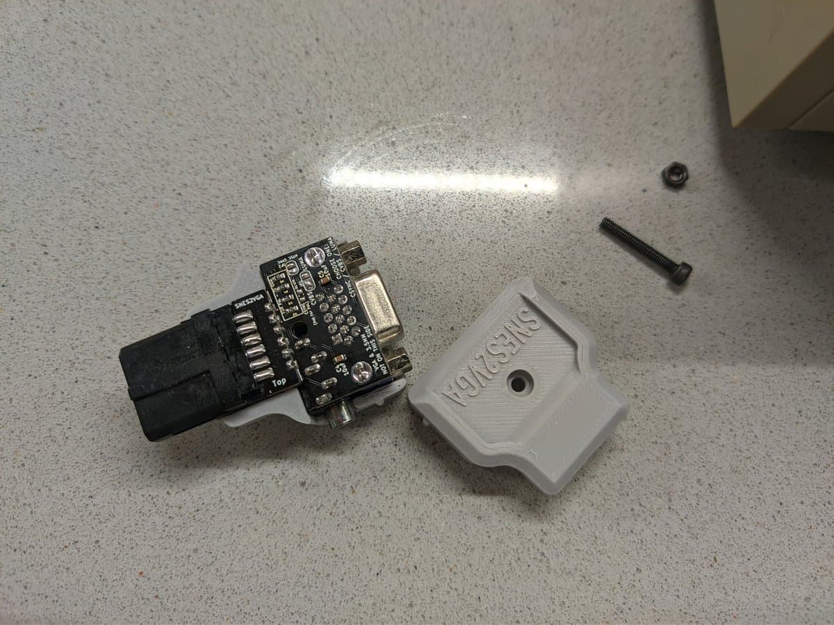 Disassembled Jeff Chen VGA dongle showing black circuit board with connectors, white plastic housing, and mounting hardware on concrete surface.
