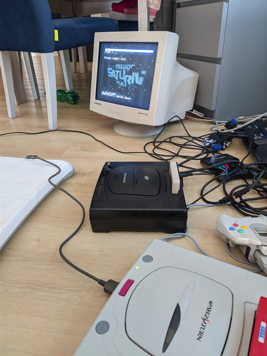 Two Jeff Chen 10DIN2VGA dongles for Sega Saturn displayed—PAL black model and NTSC white model—connected to vintage gaming setup with controllers and CRT monitor.
