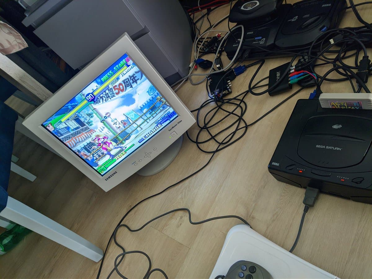 CRT monitor displaying Street Fighter Zero 3 connected to Sega Saturn via Jeff Chen VGA dongle, with controller in foreground and gaming setup on wooden desk.