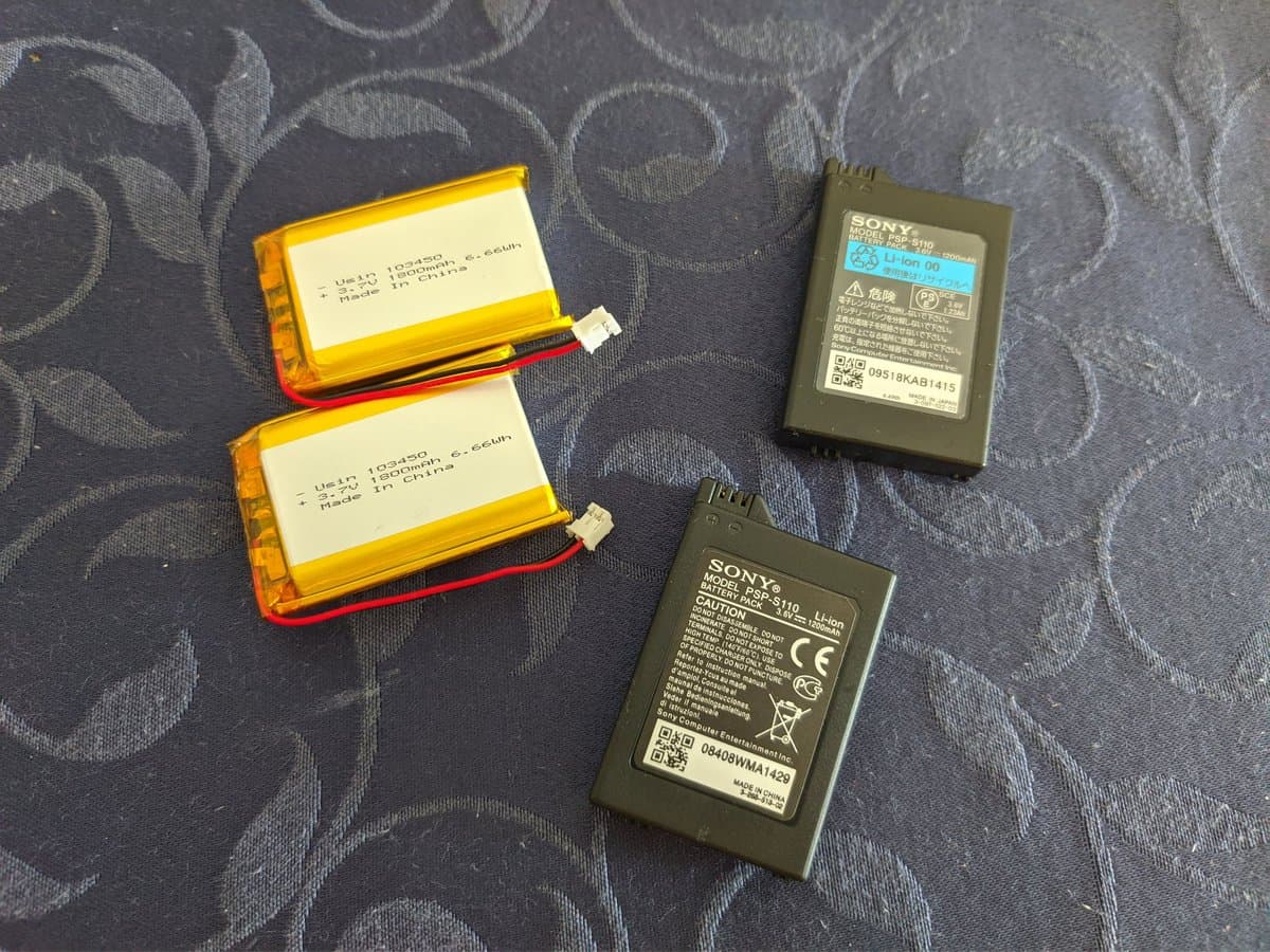 Two yellow lithium polymer batteries and two Sony PSP-3000 battery PCBs on patterned fabric; cells marked 1S2P 3.7V 1800mAh.