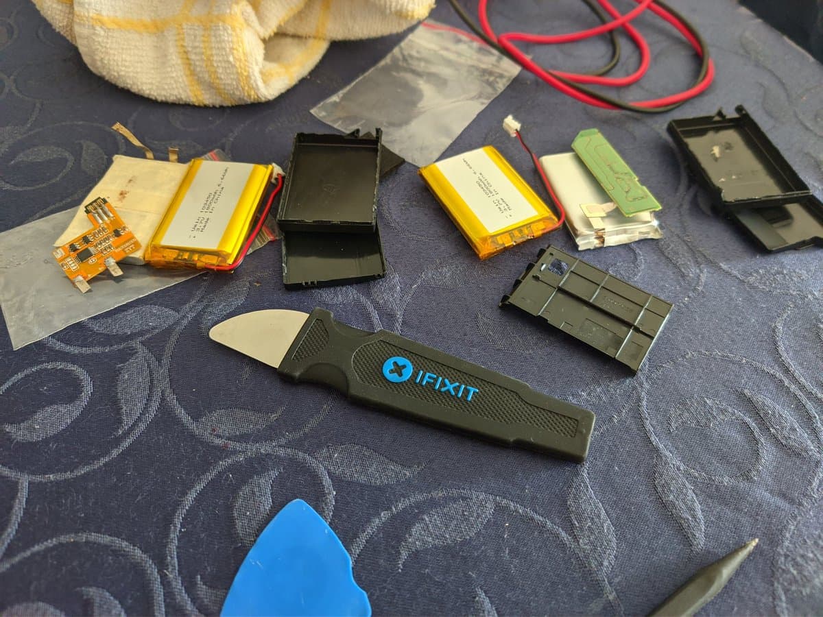 PSP-3000 battery re-celling in progress: disassembled batteries with yellow lithium cells, circuit boards, iFixit opening tool, and black battery casings on work surface.