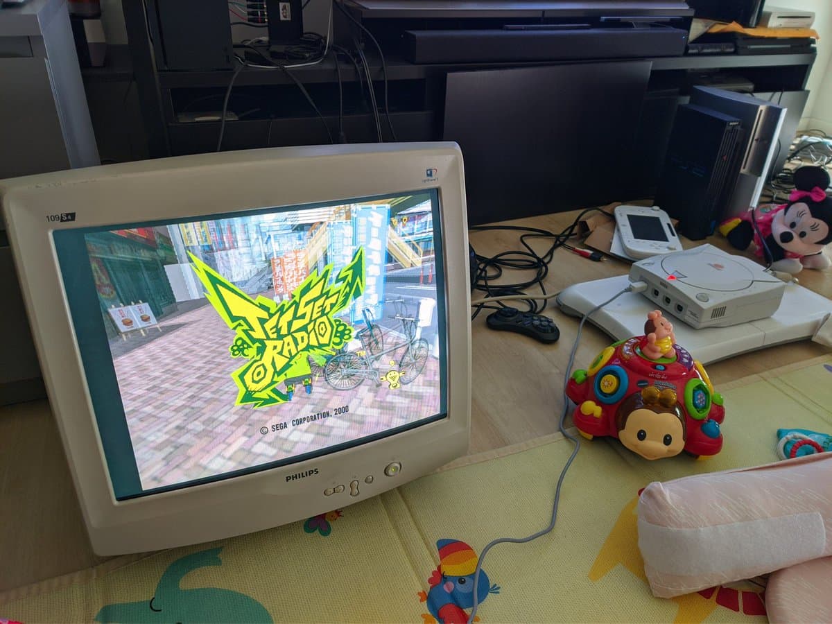 Dreamcast VA0 displaying Jet Set Radio startup screen; white gaming console and accessories on desk during GDEMU resistor mod testing.
