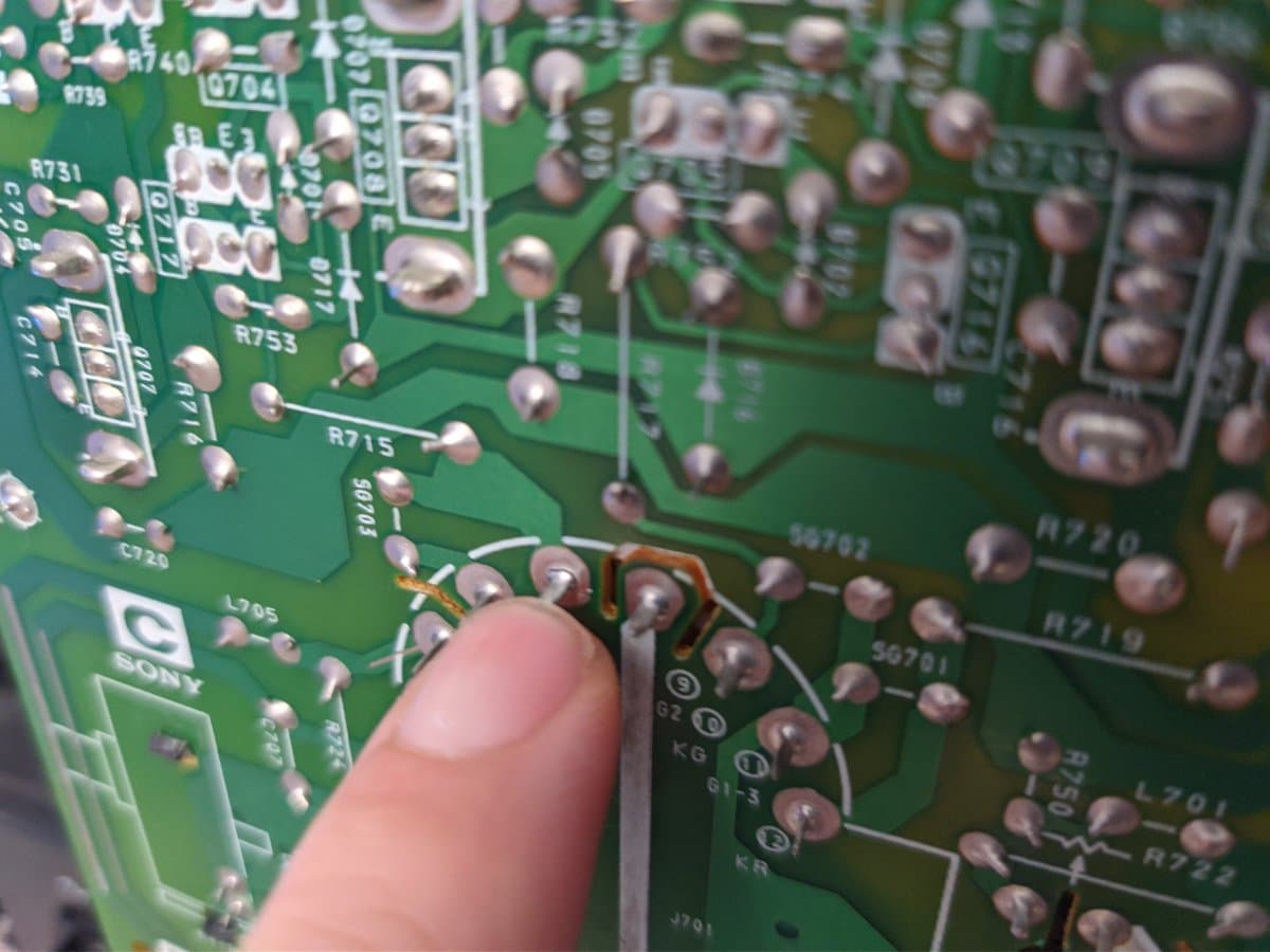 Finger pointing at broken solder joint on KB pin connector of Sony PVM-14M4J CRT tube base during blue channel repair diagnosis.