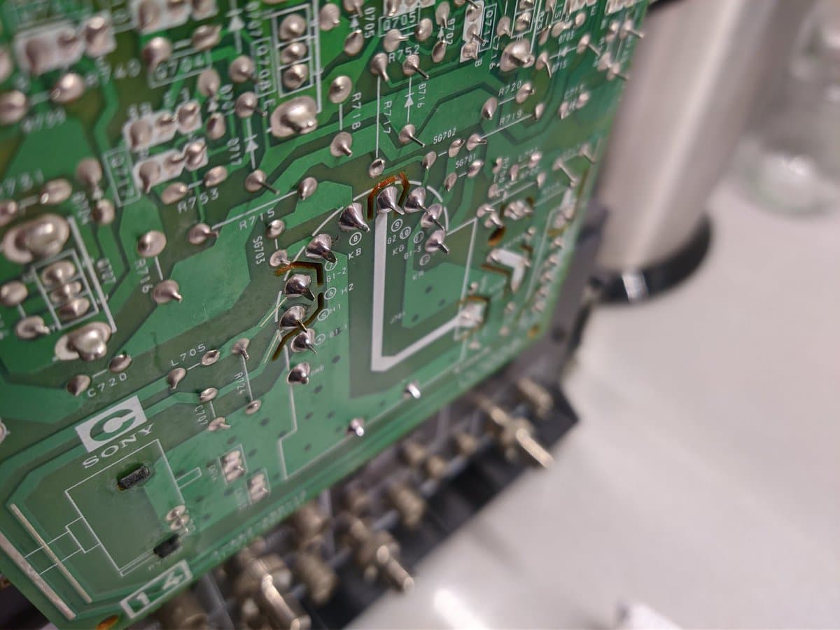 Close-up of Sony PVM-14M4J C board showing broken solder joint at KB tube pin with multimeter probe testing connection.