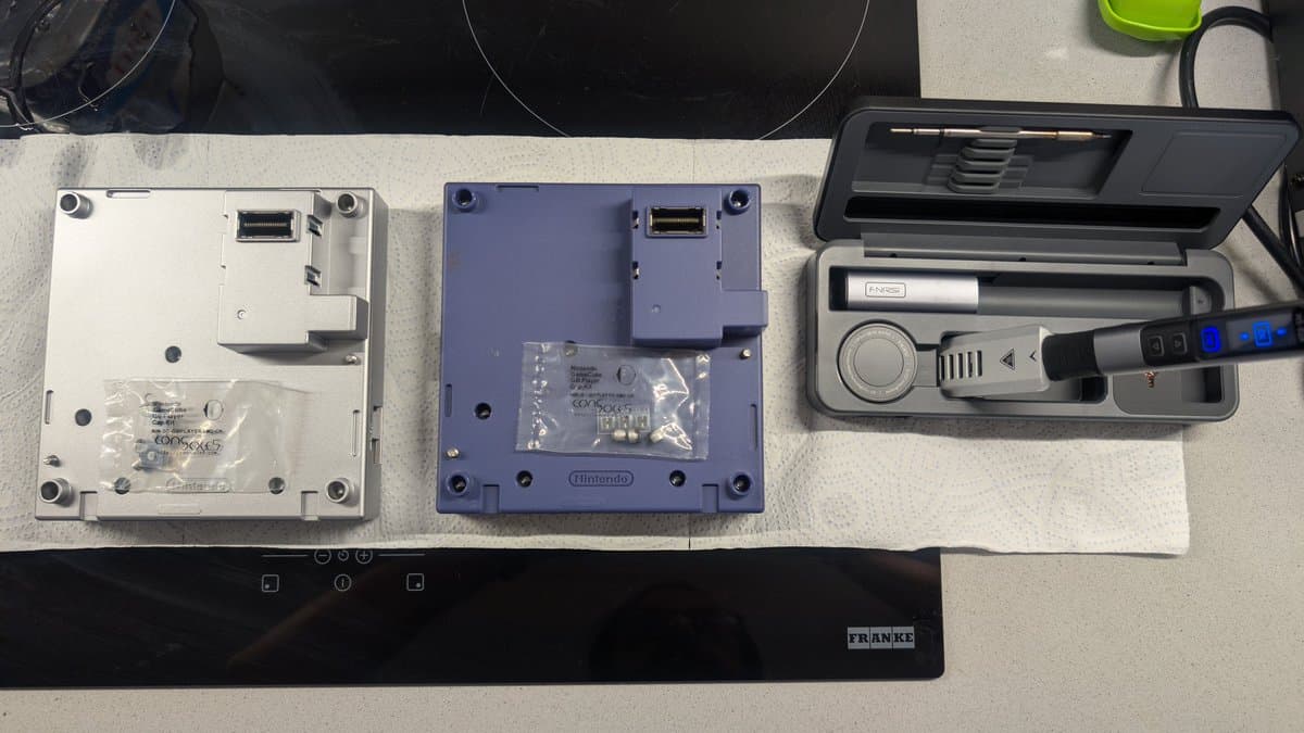 Disassembled Game Boy Player units showing back panels and internal components during recapping repair work.