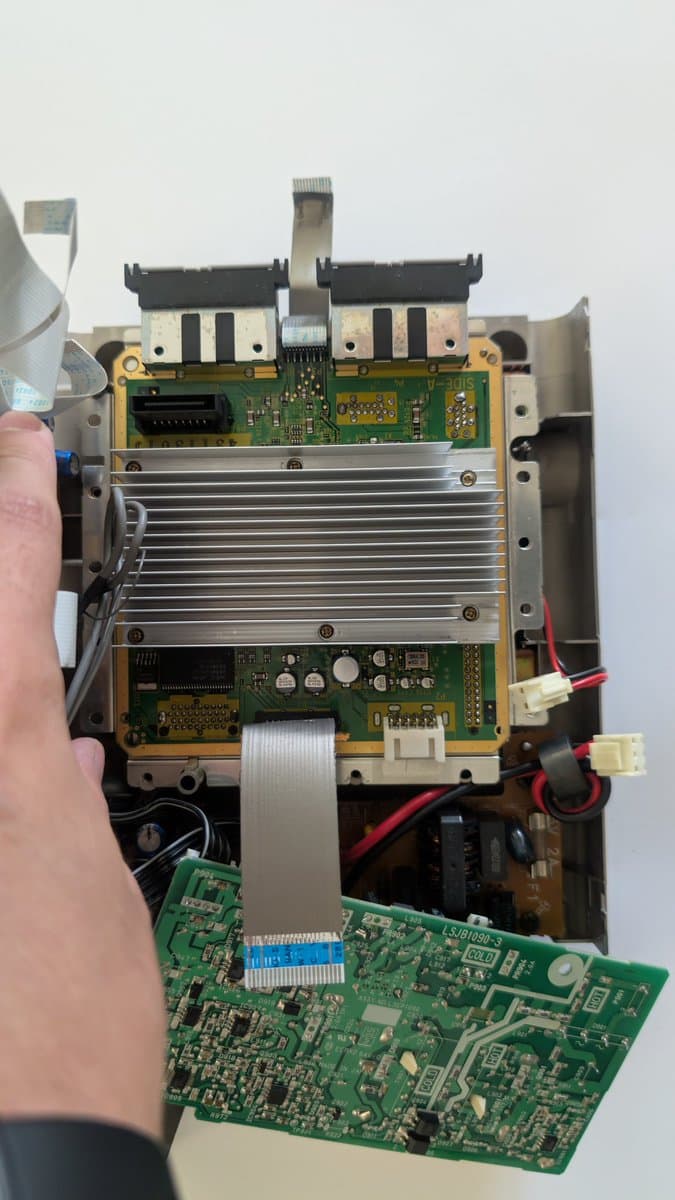 Panasonic Q motherboard being recapped, showing flex cable routing, power delivery board, and electrolytic capacitors during FlippyDrive installation.