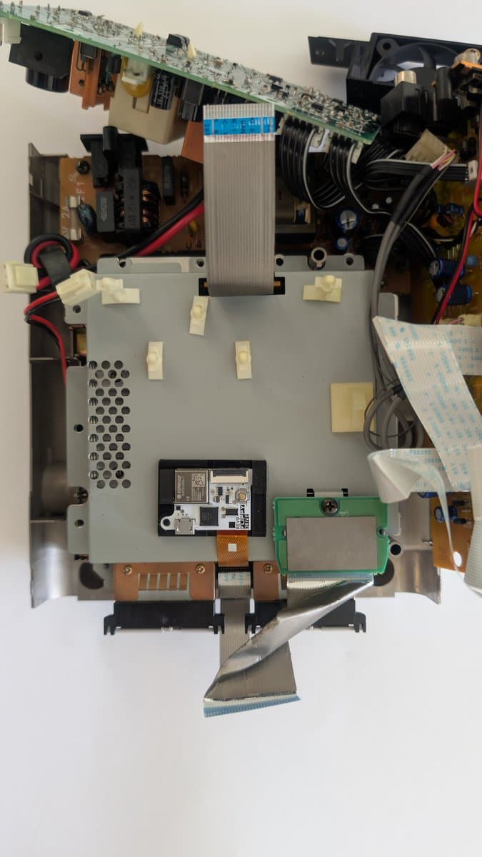 Panasonic Q motherboard interior showing FlippyDrive optical mechanism installation with flex cable routing beneath shielding, 3D printed rails visible.