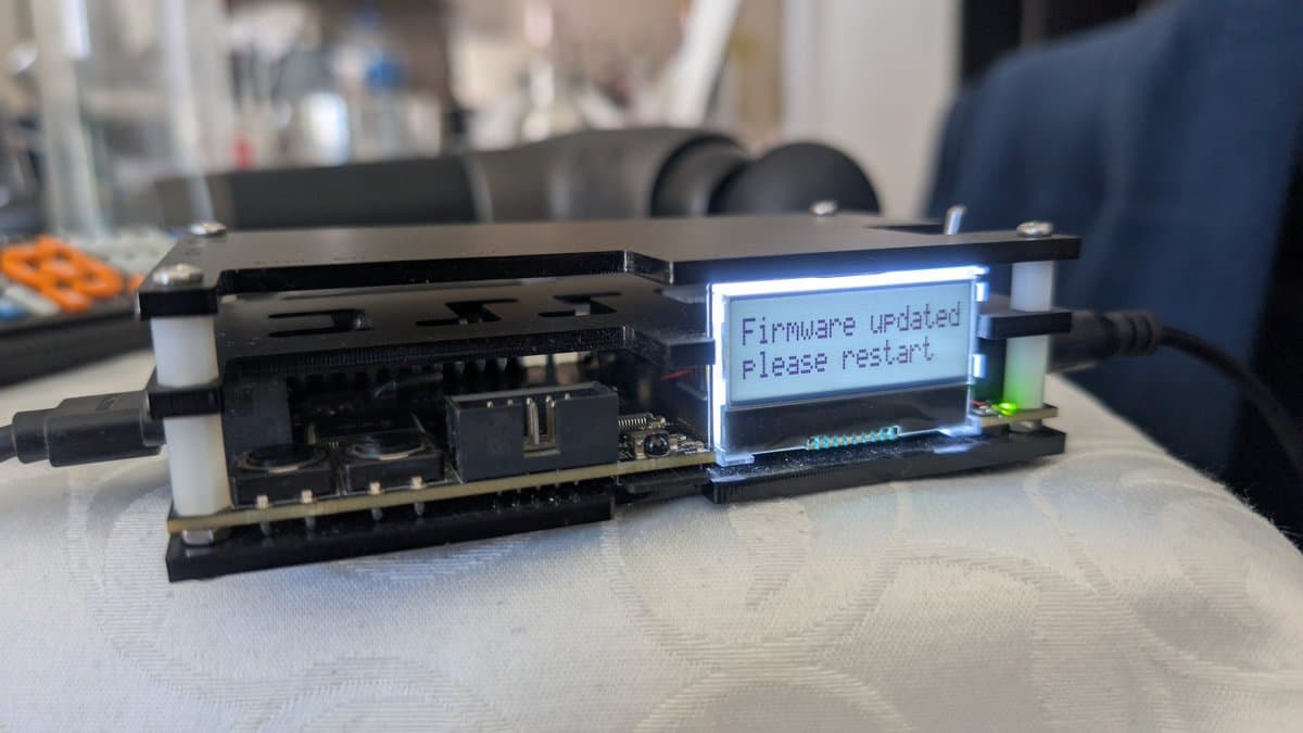 OSSC classic displaying "Firmware Updated please restart" on LCD screen during modding procedure, circuit board visible with components exposed.