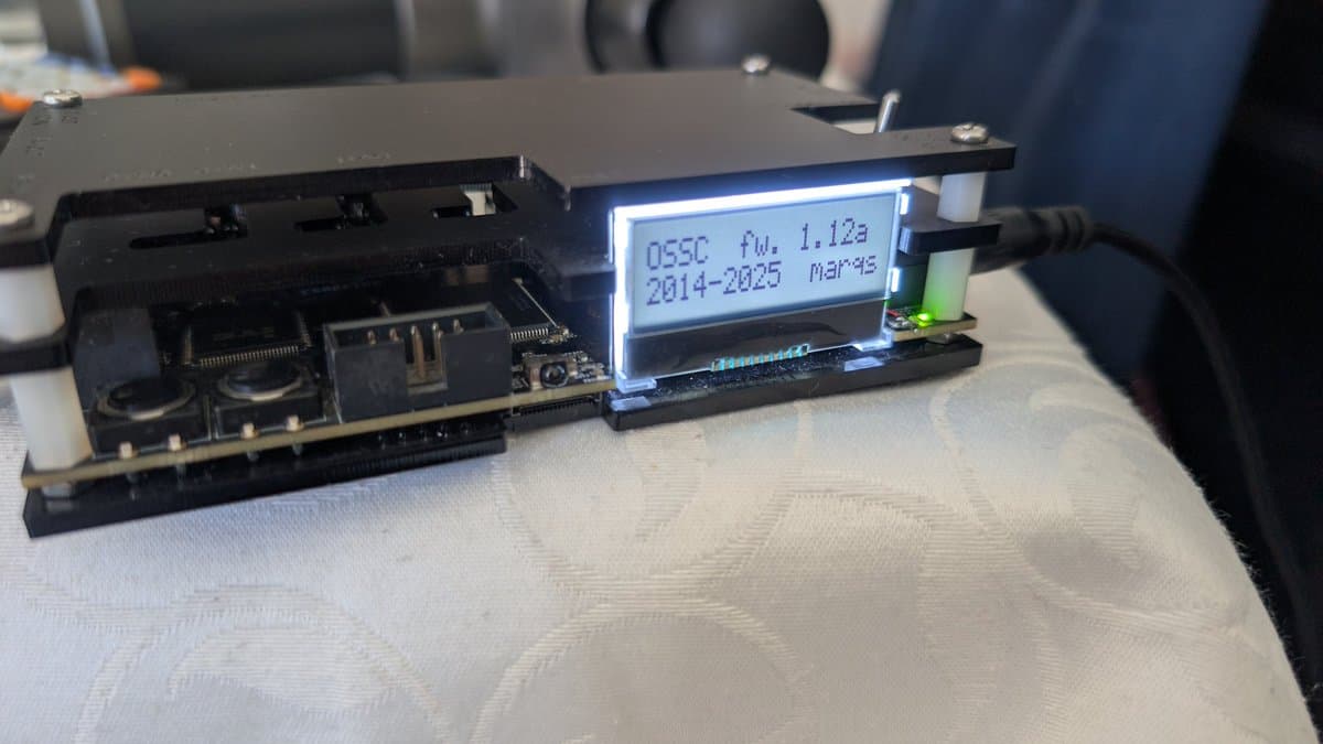 Modified OSSC board displaying firmware version 1.12a on LCD screen, with exposed PCB components and ribbon cable connections visible.