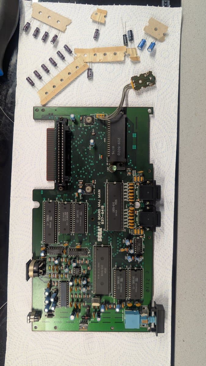 Disassembled Master System MK-2000 board with removed capacitors on wooden holders and cleaned circuit board during refurbishment.