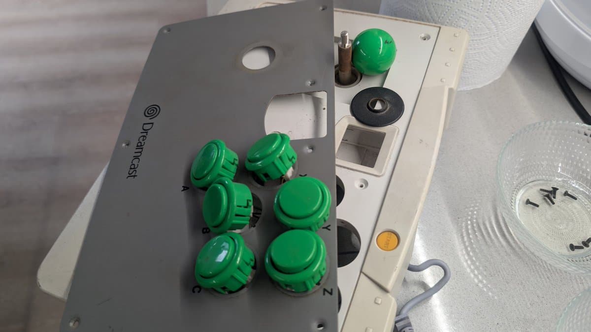 Dreamcast arcade stick with green buttons and metal panel showing "Dreamcast" branding during refurbishment restoration.