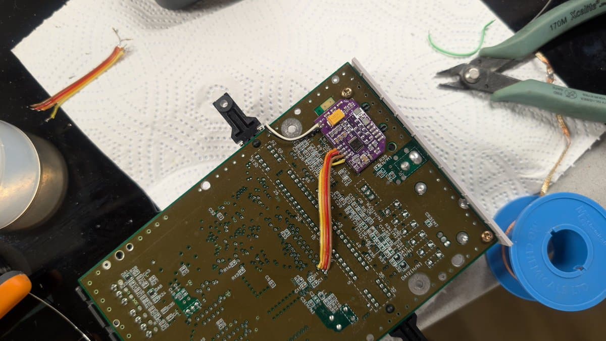 Super Famicom Jr. motherboard on workbench with purple mod board installed, soldering iron, wire strippers, and solder spool visible during repair work.