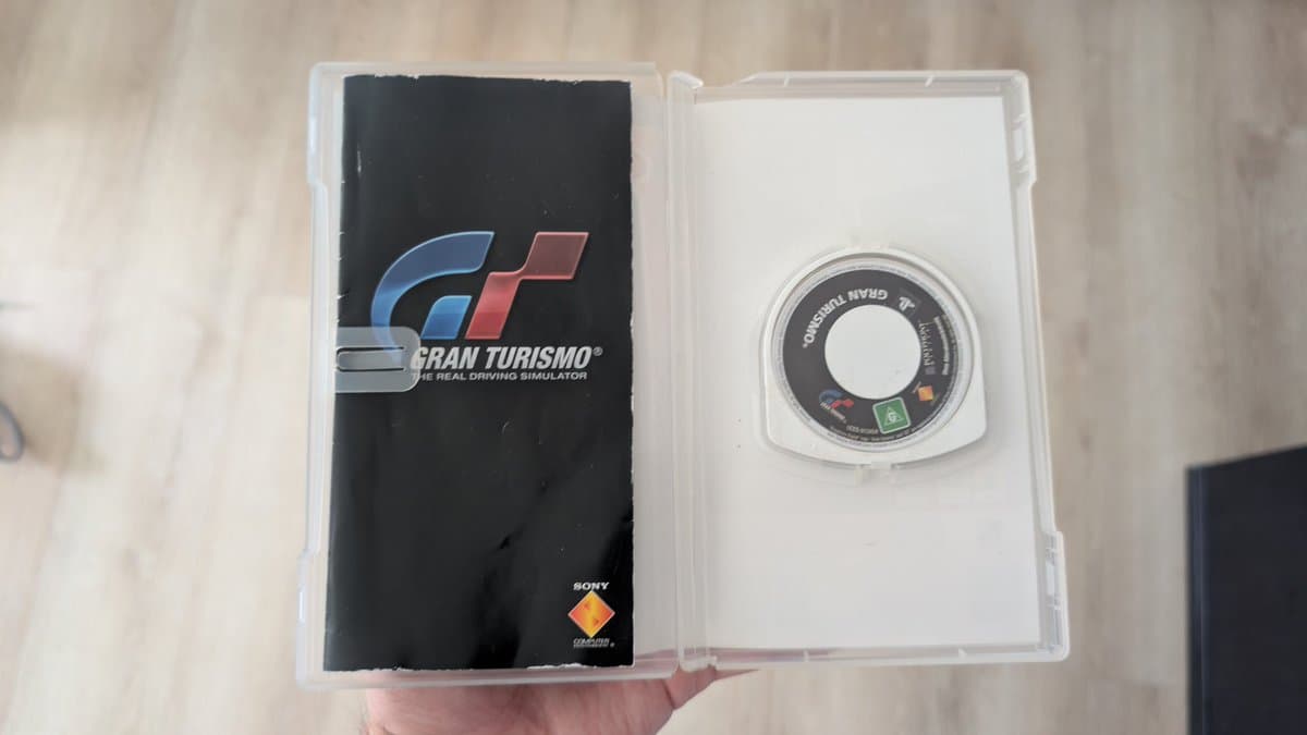 PSP Gran Turismo UMD case open showing cracked plastic shell and game disc inside clear case.