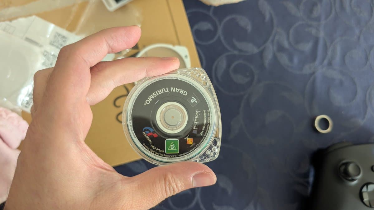 Cracked PSP UMD disc for Gran Turismo held in hand, showing damage visible on game case label.