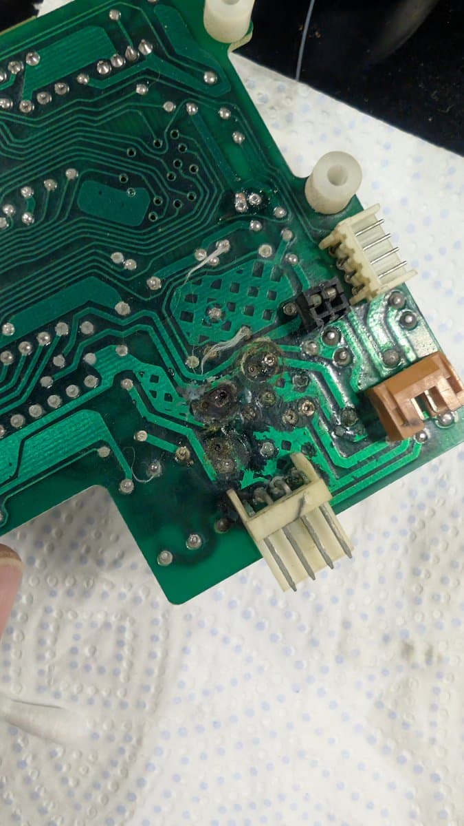 Damaged PCB section showing burned capacitor residue and charred solder joints from failed electrolytic capacitor on Sharp X68000 motherboard.