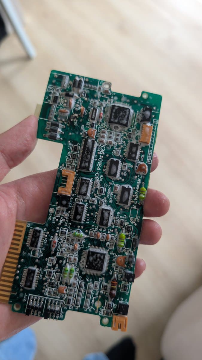Sharp X68000 circuit board held in hand, showing green PCB with IC chips, capacitors, and repaired trace work during restoration attempt.