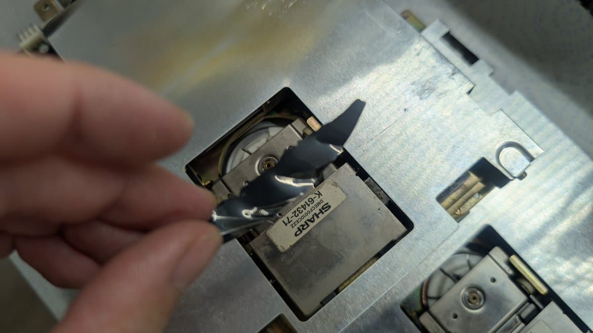 Disassembled Sharp X68000 floppy drive spindle mechanism showing broken magnetic disk fragments and damaged spindle parts during repair work.