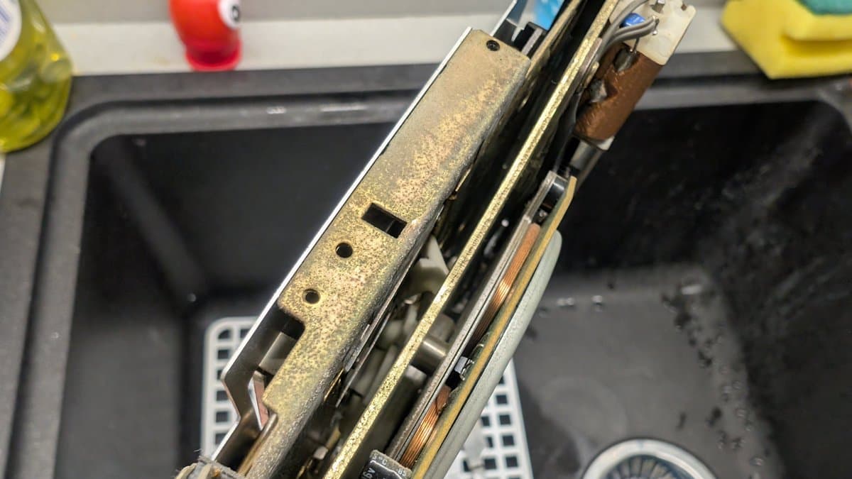 Sharp X68000 floppy drive mechanism showing damaged spindle assembly with broken pieces lodged underneath; magnetic disk debris visible.