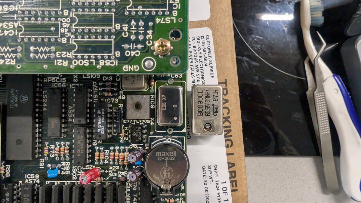 Close-up of Sharp X68000 motherboard showing new Maxell CR2032 battery, cleaned solder joints, and IC chips after oscillator replacement.