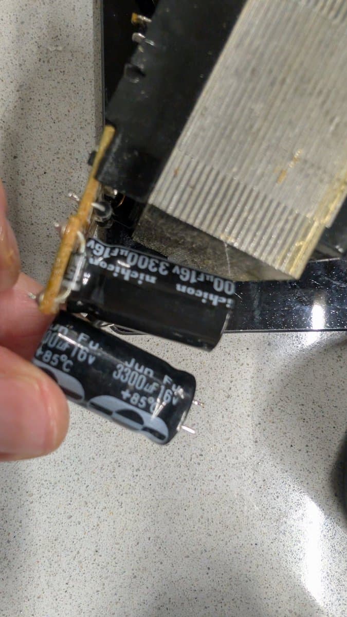 Close-up of electrolytic capacitors being replaced during Game Gear power supply recapping, showing old capacitors with visible markings next to repair work in progress.