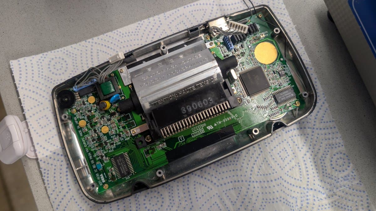 Sega Game Gear main board with capacitors removed, showing empty pads and desoldered areas on green PCB during recap repair.
