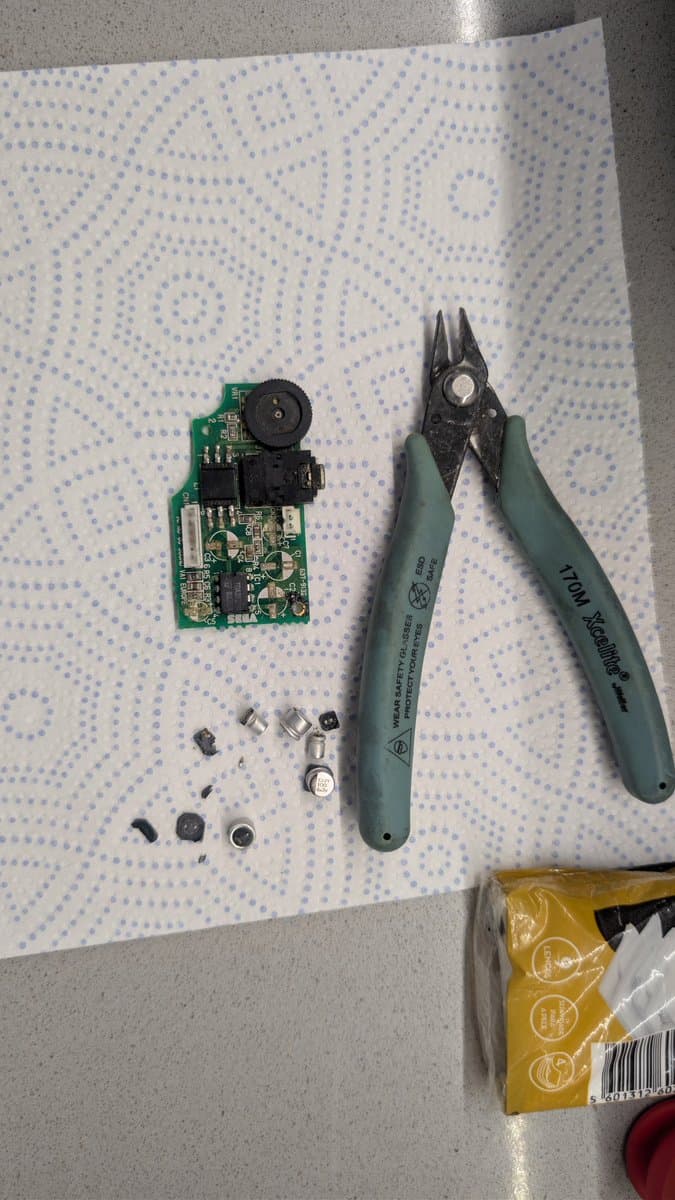 Disassembled Game Gear power board with broken solder joints, Wiha pliers, and loose components after vinegar cleaning process.