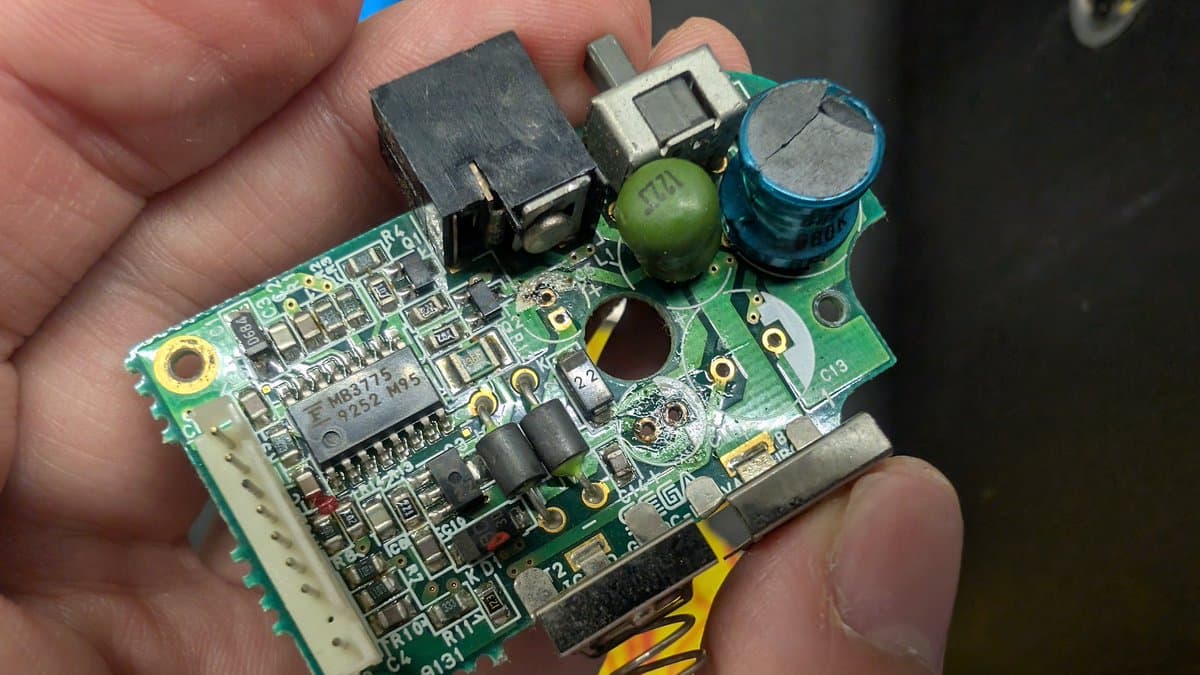 Game Gear power board held in hand showing broken solder joints at power jack after vinegar dip cleaning process.