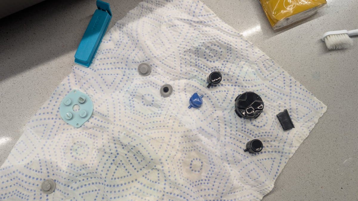 Disassembled Game Gear buttons and components laid out on dotted cloth for cleaning: rubber pad, silicone buttons, springs, and plastic casings.