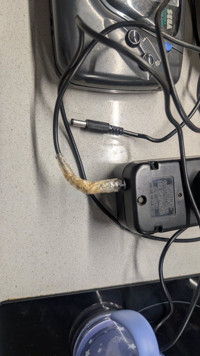 Sega Game Gear power brick with taped connection point where output cable exits casing, showing potential corrosion or damage repair.