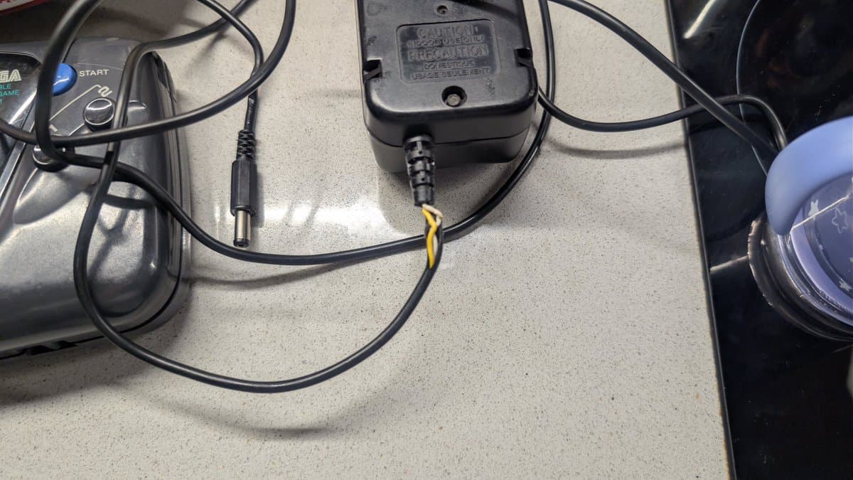 Game Gear power connector with newly soldered wires wrapped in layered heat shrink tubing, demonstrating strain relief repair technique.