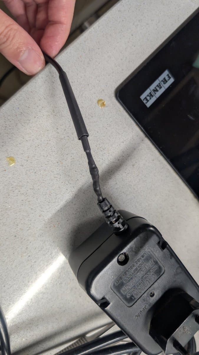 Game Gear antenna with visible solder joint repair work, held over work surface with tweezers and multimeter nearby.