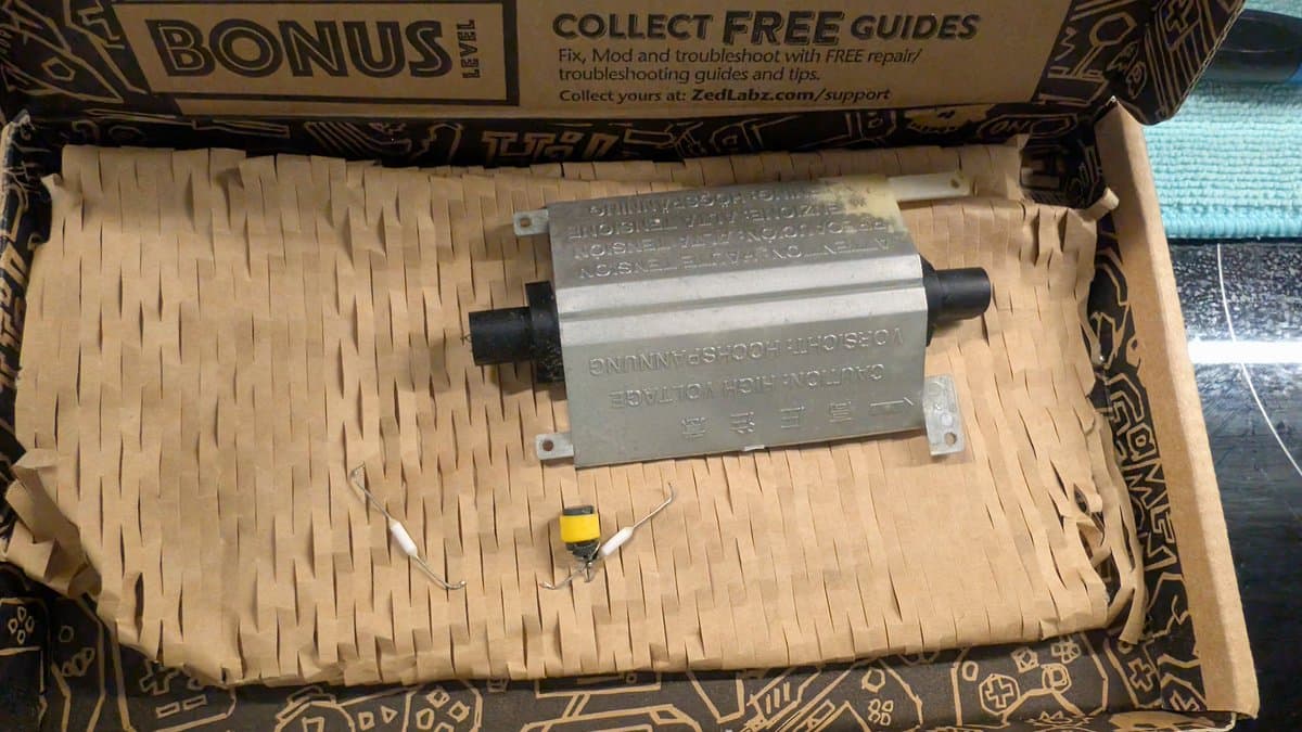 Game Gear CCFL backlight unit with metal bracket and black connectors on tan cardboard packaging with yellow capacitor visible.