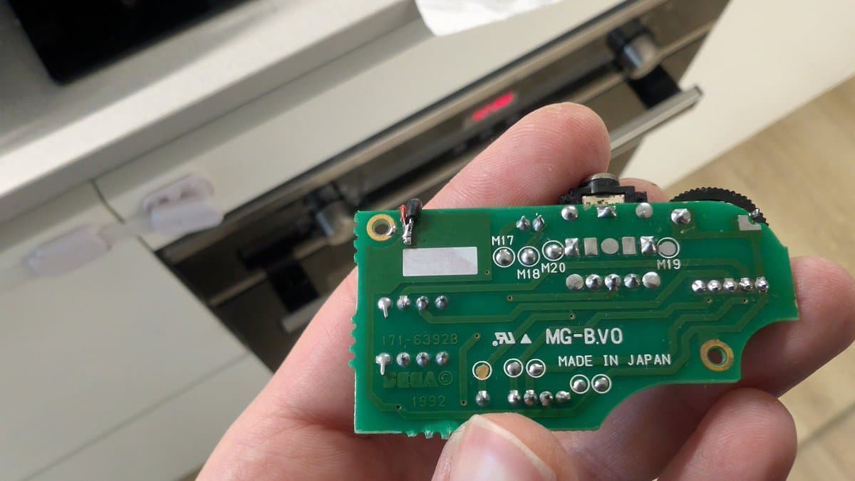 Close-up of Sega Game Gear MG-BV0 audio board held in hand, showing broken vias on ground plane near component labels M17-M20 and M19.
