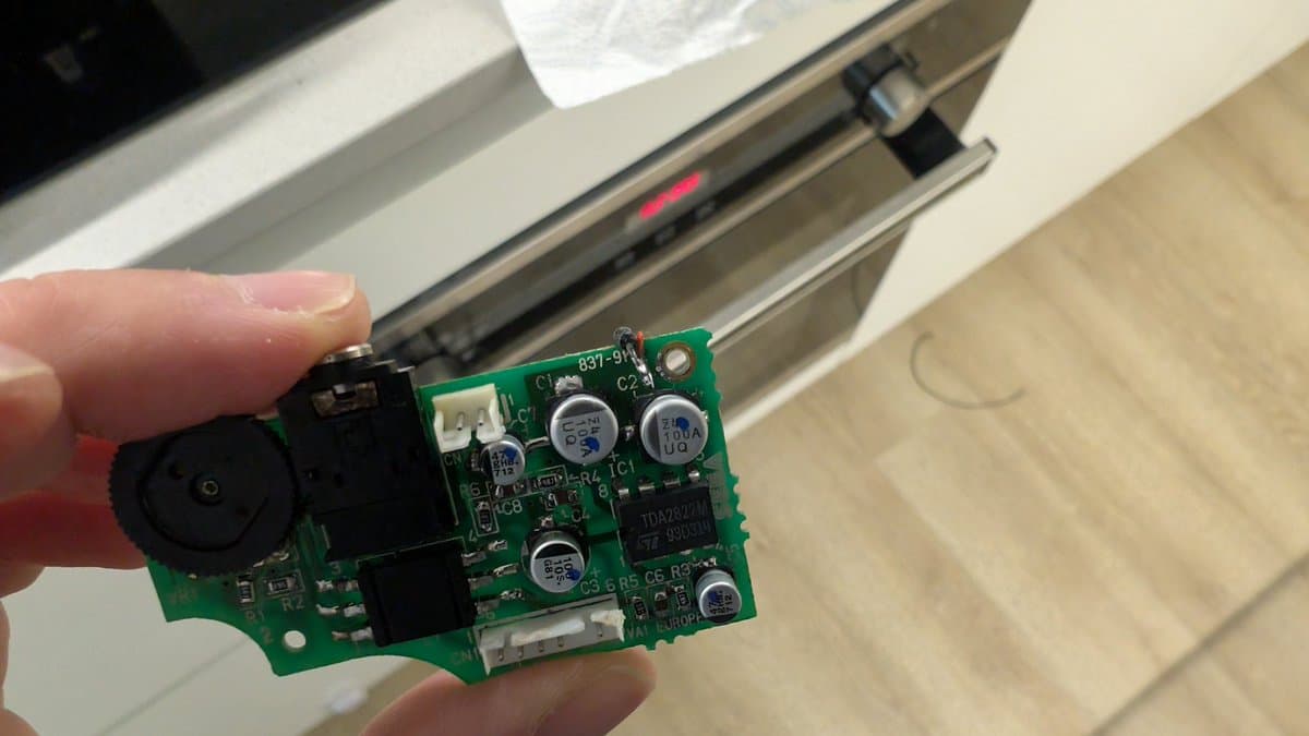 Close-up of Game Gear audio circuit board held in hand, showing broken vias on ground plane and electrolytic capacitors.