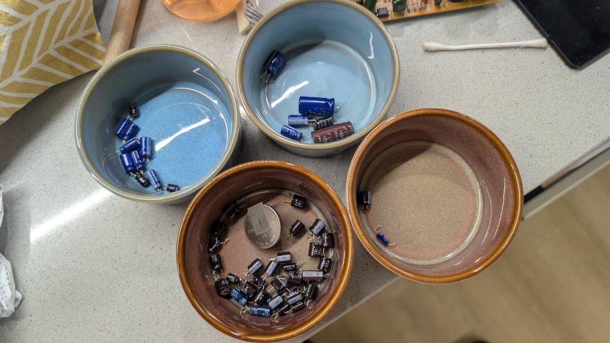 Four bowls of capacitors sorted by type during FM Towns Marty recap; blue and brown containers hold electrolytic capacitors removed from the console.