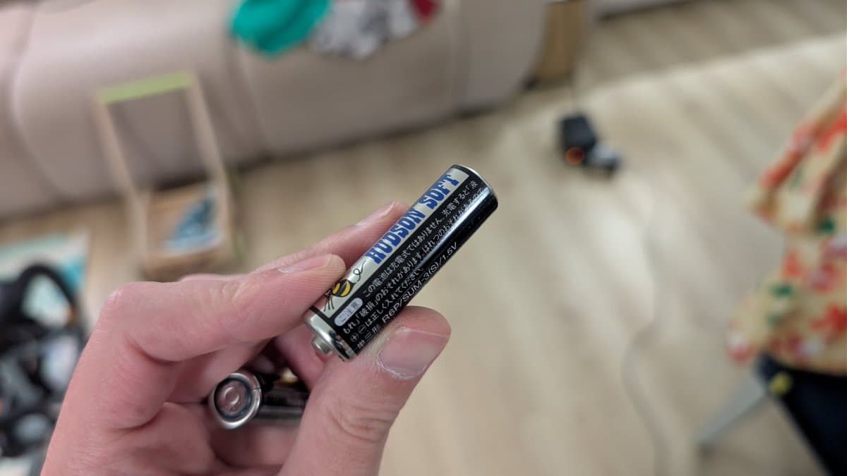 Hand holding original Hudson Soft branded AA battery from Ten No Koe 2, with discharged battery visible below.