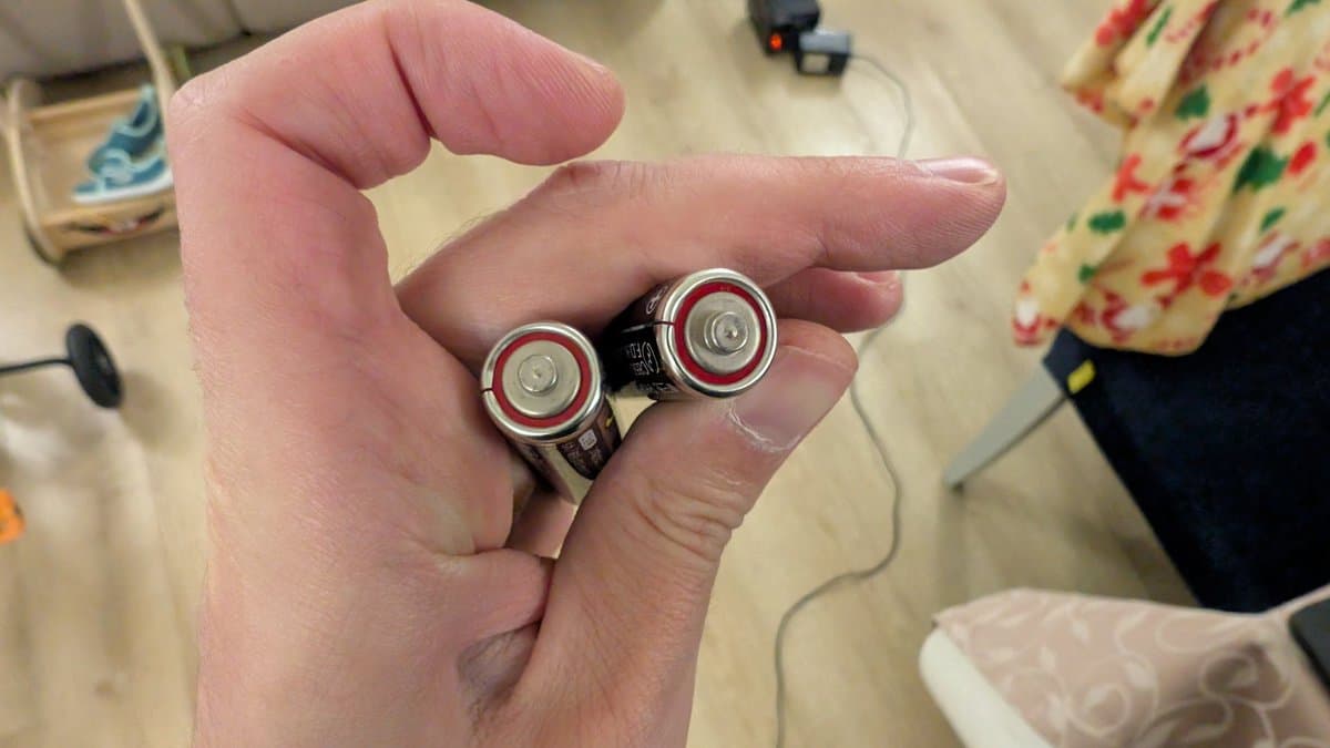 Close-up of two Hudson Soft branded AA batteries held in palm, showing original factory components from Ten No Koe 2 handheld device.